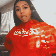 a woman wearing a red hoodie with the word aas on it sticking her tongue out