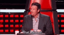 a man in a suit is sitting in a chair with a cup of coffee and a button that says that was hot .