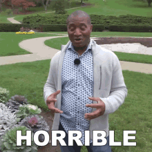 a man in a polka dot shirt is standing in front of a garden and the word horrible is above him