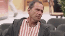 a man in a striped shirt is sitting in a row of chairs and making a face .