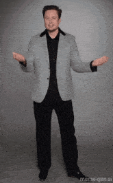 a man in a grey jacket and black shirt is standing with his arms outstretched in front of a meme-gen.ai logo