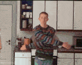 a man in a colorful sweater is standing in a kitchen