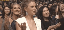 a woman in a white dress is sitting in a crowd of people applauding and smiling .