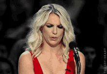 a woman in a red dress stands in front of a microphone with trashy heart written on the bottom right