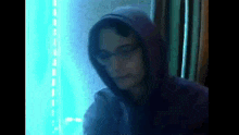 a man wearing a purple hoodie and glasses is standing in front of a blue light .