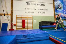 a man is jumping on a balance beam in front of a wall that says the rules of circus