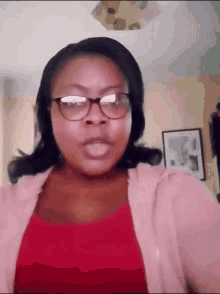 a woman wearing glasses and a pink shirt is making a funny face .