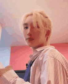 a young man with blonde hair is standing in front of a pink wall and smiling .