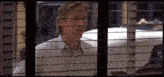 a man in a striped shirt is looking out of a window with blinds .