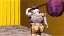 a cartoon character is walking down a sidewalk carrying a large ball on his back .