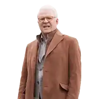 an older man wearing glasses and a brown coat stands in front of a white background