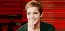 a woman with short hair is smiling with her hand on her chin .