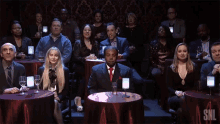 a group of people sitting at tables with a snl logo on the bottom right