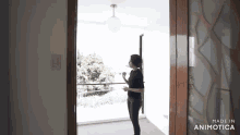 a woman is standing on a balcony looking out the window and talking on a cell phone .