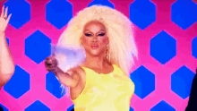 a drag queen in a yellow dress is pointing at the camera