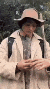 a man wearing a hat and a coat is holding a stick in the woods .