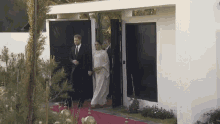 a man in a suit and tie and a woman in a white dress are walking on a red carpet .