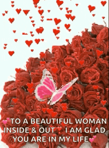 a pink butterfly is flying over a bouquet of red roses .
