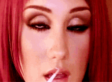 a close up of a woman with red hair applying lip gloss