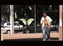 a shirtless man walking down a street in front of a phone booth