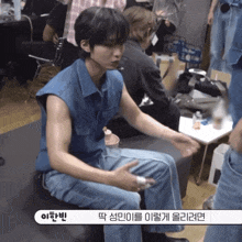 a man in a blue vest is sitting on a couch with korean writing on the bottom