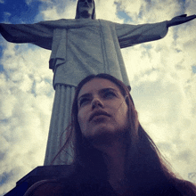 a woman is standing in front of a large statue of jesus