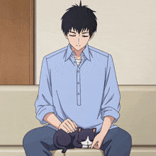 a man in a blue shirt sits on a couch petting a black cat