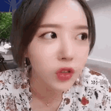 a close up of a woman making a funny face while wearing a floral shirt .