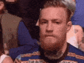 a man with a beard is sitting in a crowd of people looking at something .