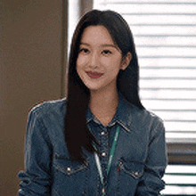 a woman wearing a denim shirt and a lanyard is sitting in front of a window .