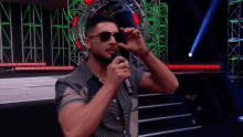 a man wearing sunglasses and a hat holds a microphone in his hand