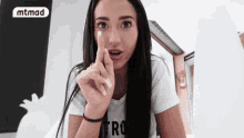 a woman wearing a white t-shirt with the word tro on it holds her finger to her lips