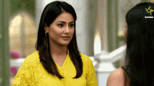 a woman in a yellow dress stands next to another woman with a hotstar logo in the corner