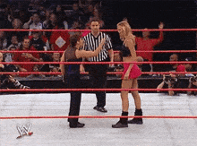 two women are wrestling in a wrestling ring while a referee stands between them .