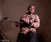 a man in a floral shirt is holding a hammer in his right hand .