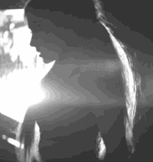 a black and white photo of a woman with long hair looking at a cell phone .