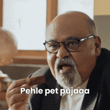 a man with glasses and a beard is holding a piece of food and the words pehle pet pujaaa are above him