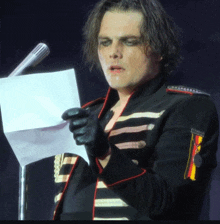 a man holding a piece of paper in front of a microphone while wearing a black and red jacket