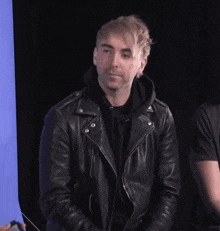 a man wearing a black leather jacket and a black hoodie is smiling
