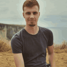a man with a beard wearing a grey shirt is sitting on the ground