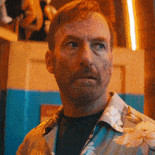a man with a beard and a floral shirt looks at the camera