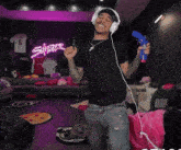 a man wearing headphones is holding a toy gun in front of a neon sign that says fly emirates on it