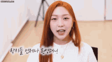a woman with red hair is smiling and waving her hand in a video .