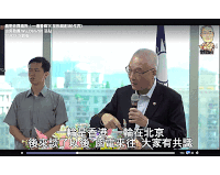 a man in a suit is speaking into a microphone while another man looks on