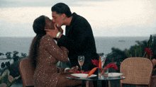 a man and a woman are kissing at a table with wine glasses