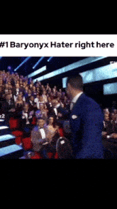 a man in a blue suit is standing in front of a crowd of people and says # 1 baryonyx hater right here