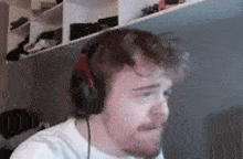 a man wearing headphones and a white shirt is sitting in front of a computer screen .