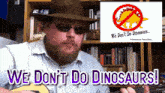 a man playing a guitar with the words we do n't do dinosaurs behind him