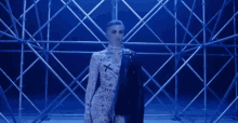 a woman in a jumpsuit and a leather jacket is standing in front of a scaffolding structure .