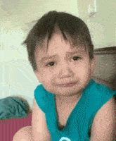 a little boy in a blue shirt is crying and making a funny face .
